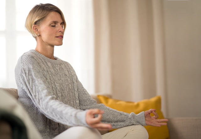 Person sitting peacefully with eyes closed, practicing gentle breathing at home.